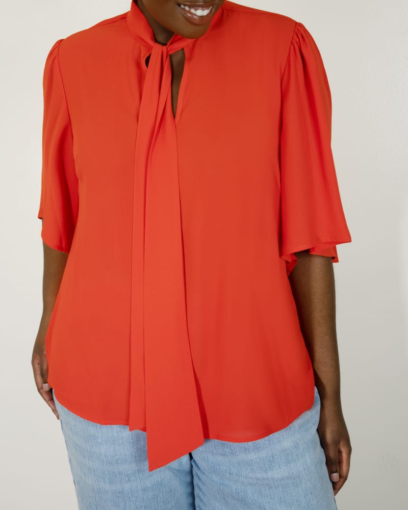 Side of a model wearing a size 28 Bow Blouse with Flutter Sleeve in Valiant Poppy by ELOQUII. | dia_product_style_image_id:295104